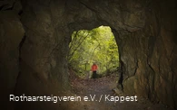 Zwei Wanderer die durch einen höhlenartigen Tunnel gehen